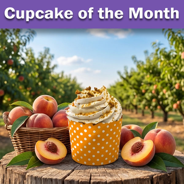 Cupcake of the Month: A white frosted cupcake in an orange polka dot wrapper topped with buttery streusel, surrounded by fresh peaches in a wicker basket against a sunny peach orchard backdrop.